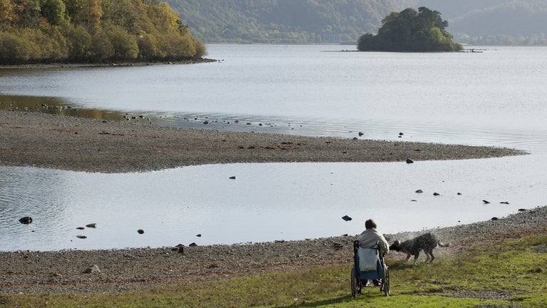 A wheelchair user and her dog enjoying the view across Derwent Water from the shore